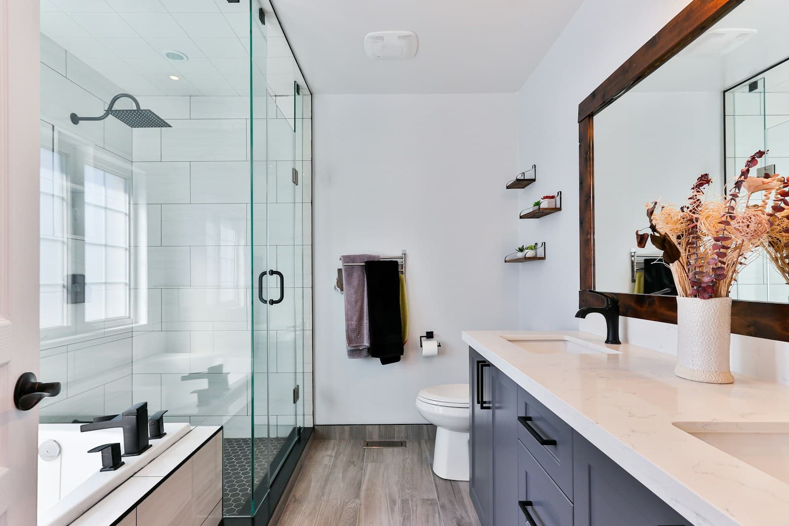 Remodeled bathroom with a frameless glass shower, white tile, matte black fixtures, and a wood-framed mirror