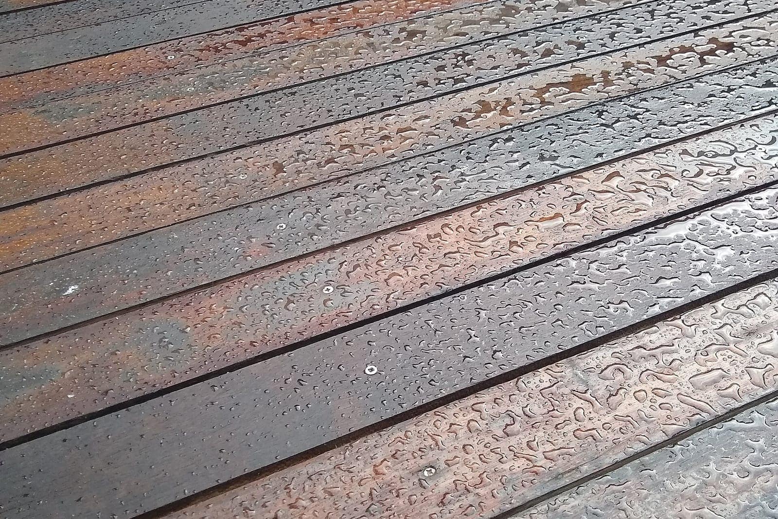 Close-up of weathered hardwood deck boards with exposed screws and rain beading on the surface