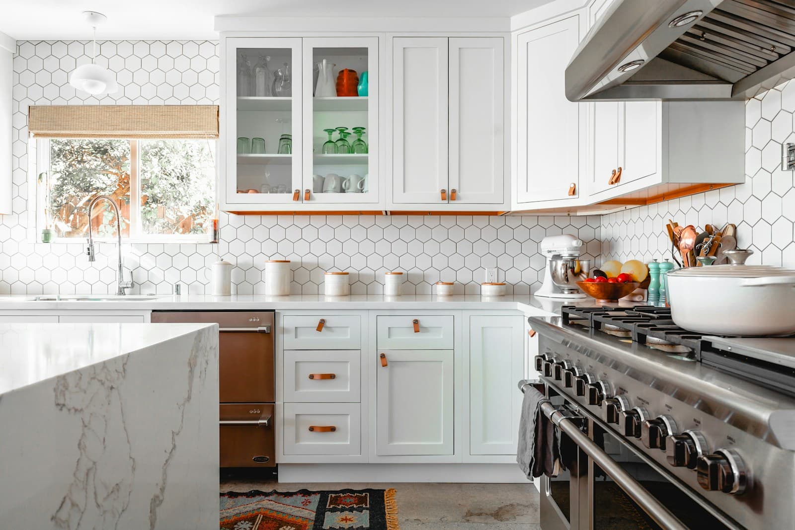 Bright kitchen with white shaker cabinets, a marble-topped island, hexagon tile backsplash, and a professional-style range