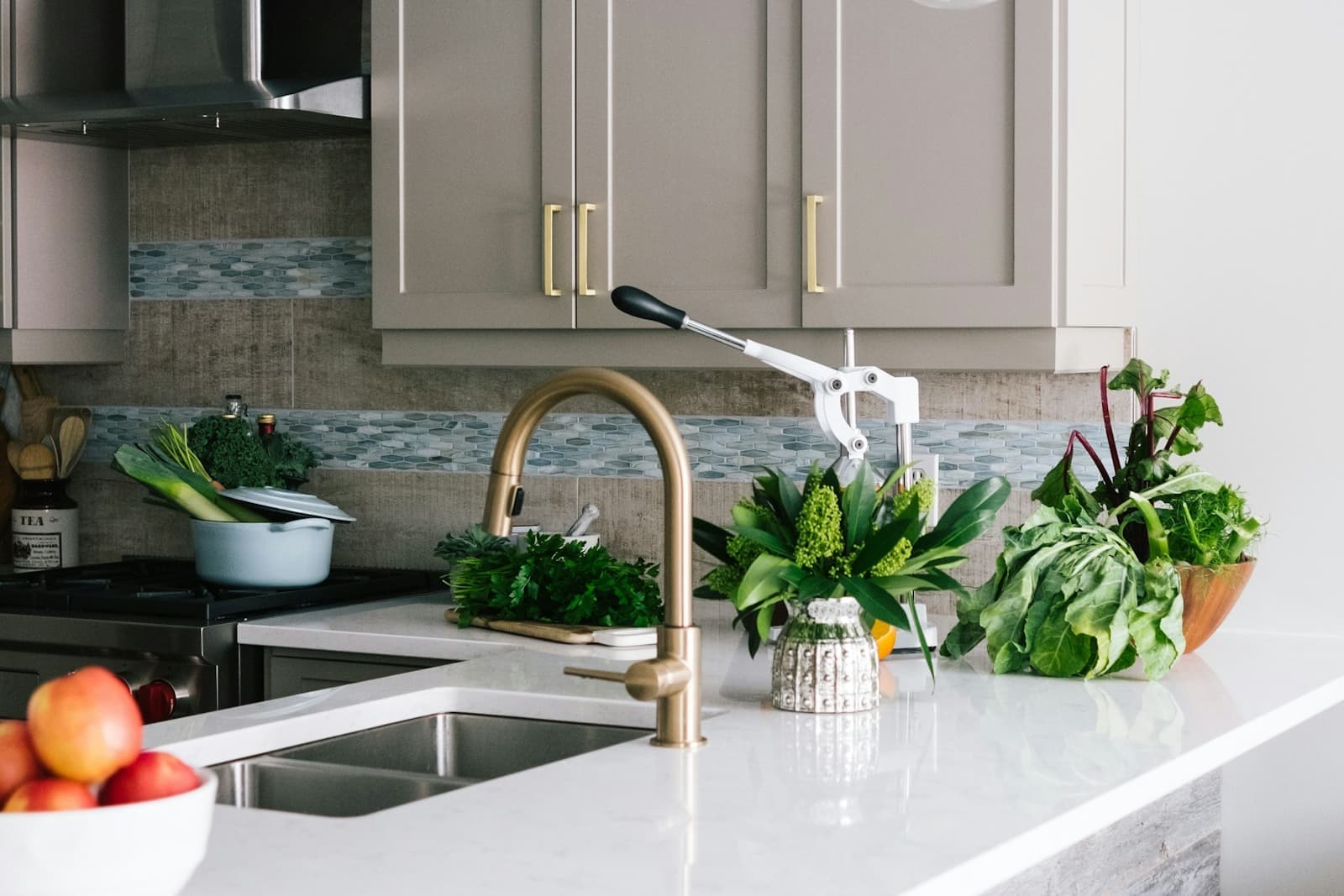 Close-up of an undermount kitchen sink with a brass faucet, white countertop, and mosaic tile backsplash