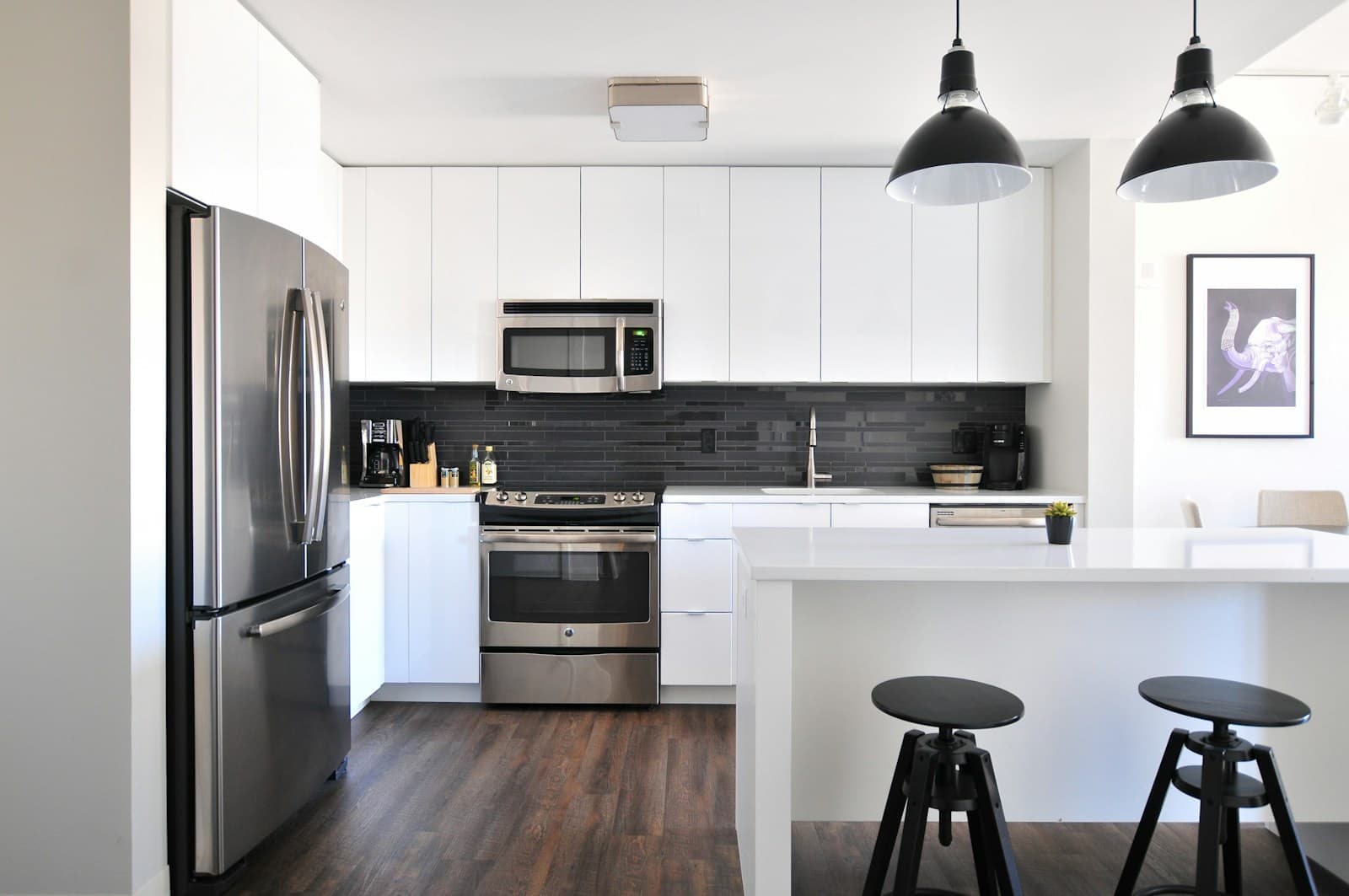 Modern kitchen with white flat-panel cabinets, stainless steel appliances, dark tile backsplash, and an island with bar stools