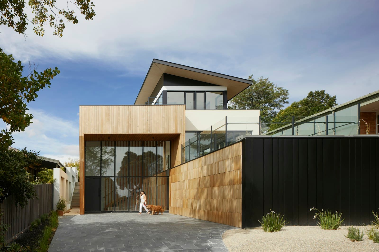 Contemporary two-story home with wood and dark siding, large windows, and a gravel front yard